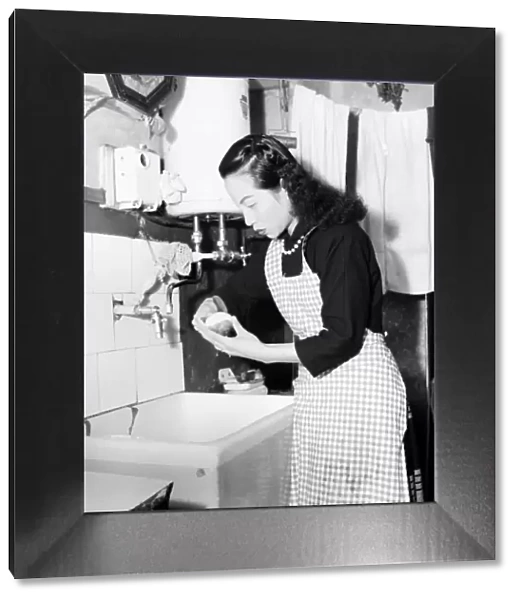 Domestic Scenes A woman peeling potatoes in her kitchen sink, getting dinner ready
