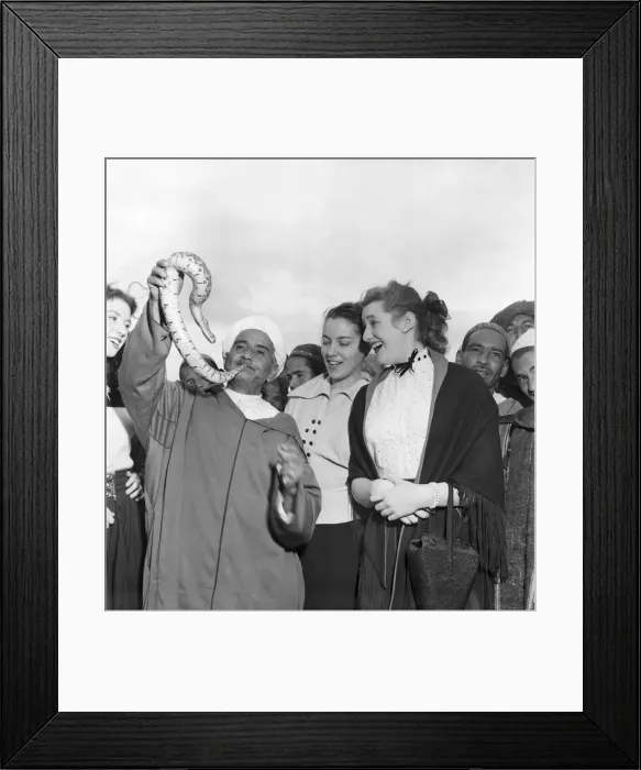 Framed Print : Local man of North Afric holding up a snake with a group of women gathered around to Framed Print : Local man of North Afric holding up a snake with a group of women gathered around to