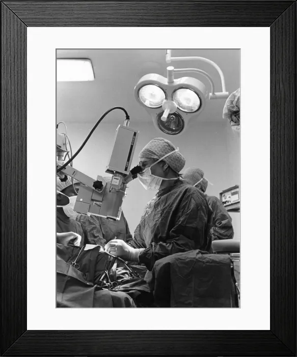 Framed Print : A surgeon looks through the microscope as she works on the patient Framed Print : A surgeon looks through the microscope as she works on the patient