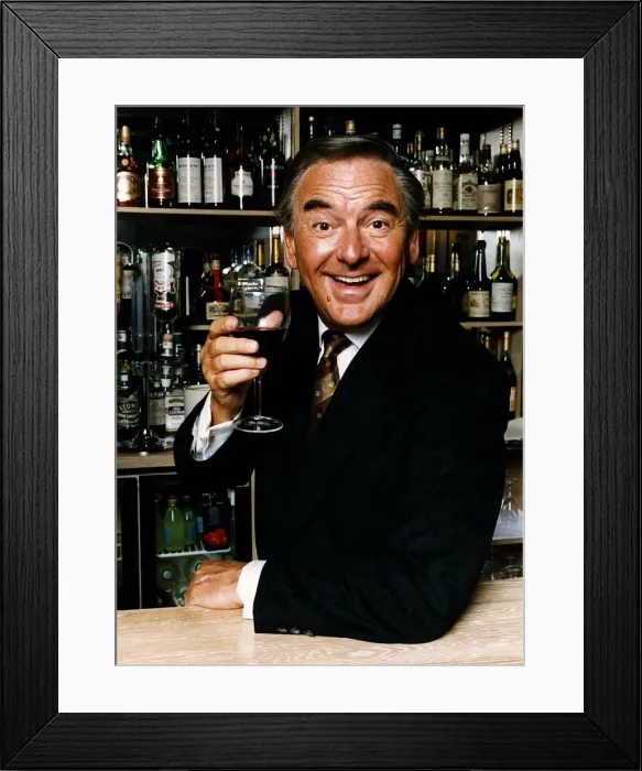 Framed Print : Bob Monkhouse raises a glass of wine standing behind a well stocked bar Framed Print : Bob Monkhouse raises a glass of wine standing behind a well stocked bar