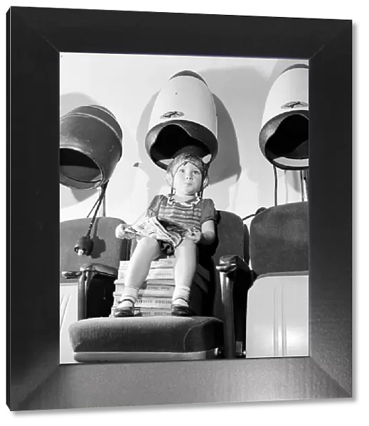 Young girl sitting with her head under a dryer at her local hairdressers August