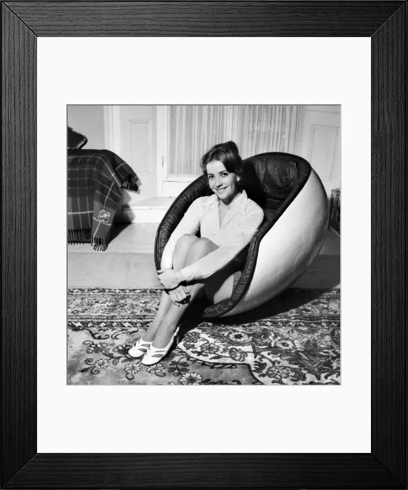 Framed Print : Woman sitting in an egg chair wearing white blouse and black skirt