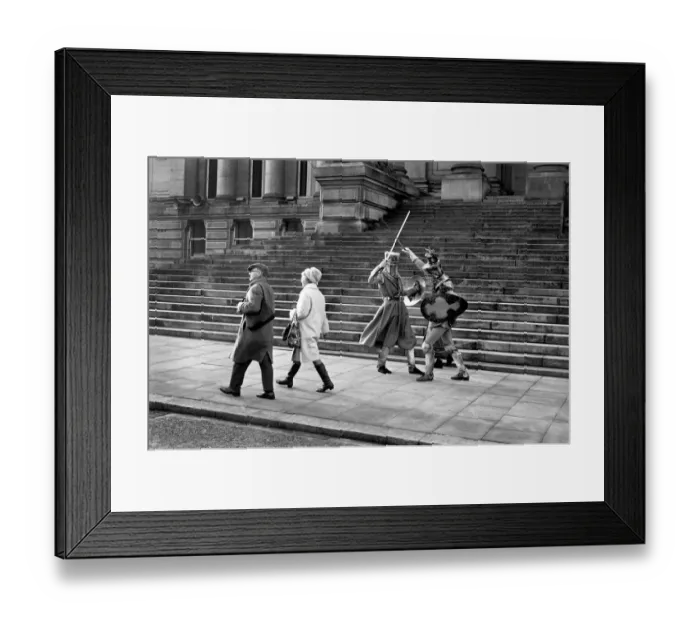 Framed Print : Shoppers hurry past the Town Hall steps as a couple of medieval knights are locked in