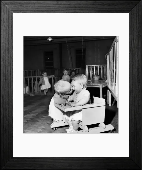 Framed Print : Children playing at a day nursery in Leeds. One sitting in the chair as another toddler Framed Print : Children playing at a day nursery in Leeds. One sitting in the chair as another toddler