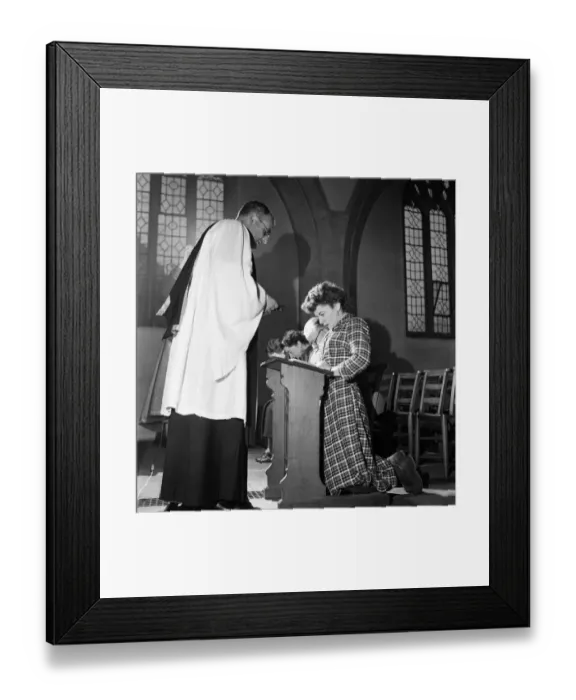 Framed Print : Woman kneeling at the altar praying in church watched by her priest December 1952