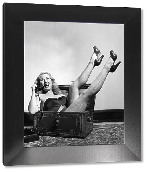 Actress June Cochrane sitting in a chest talking on the telephone. October 1952 C5181