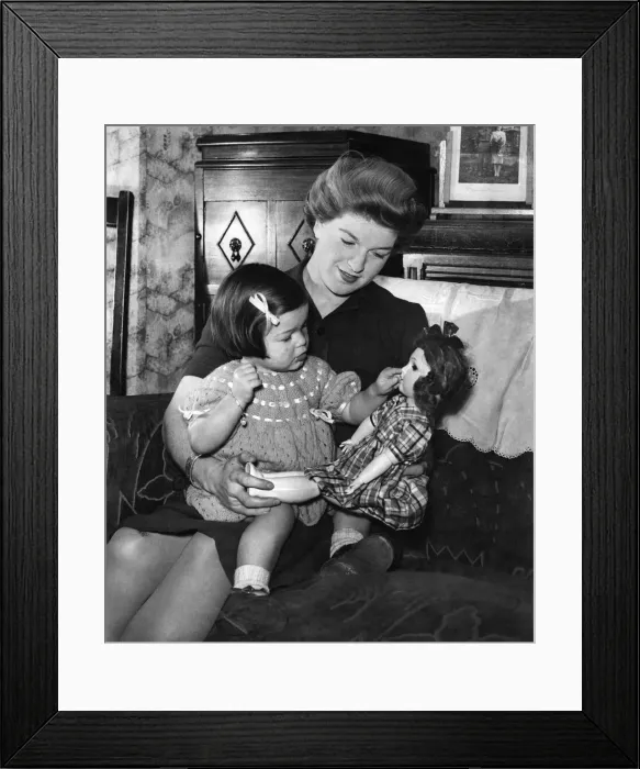 Framed Print : Mother and child at home, the girl playing with her doll as she sits on mummys lap Framed Print : Mother and child at home, the girl playing with her doll as she sits on mummys lap