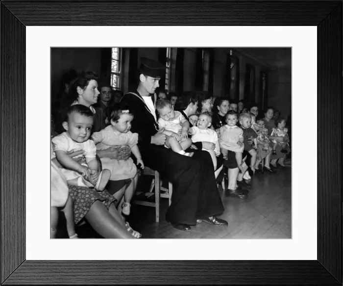 Framed Print : A sailor sits in a hall with his child on his lap with a room full of mothers