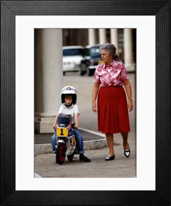Framed Print : Prince Harry wearing crash helmet and sitting on a toy motorcycle with woman by his side Framed Print : Prince Harry wearing crash helmet and sitting on a toy motorcycle with woman by his side