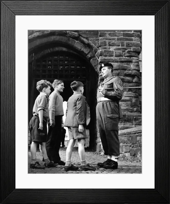 Framed Print : This patient sergeant answers the many questions of these young lads at the gate of Framed Print : This patient sergeant answers the many questions of these young lads at the gate of