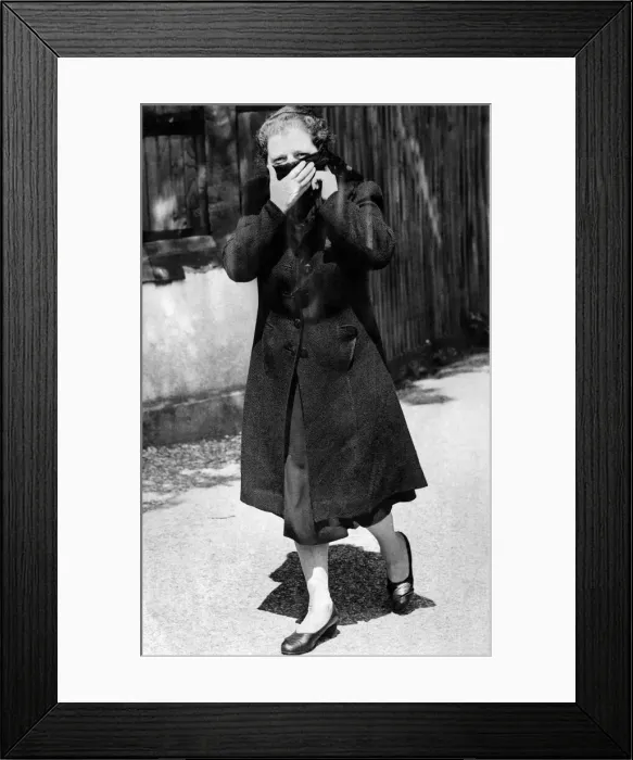 Framed Print : Woman walking down the street wearing a long over coat and turning up the collar to cover
