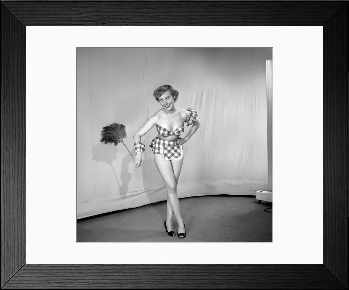 Framed Print : Woman wearing plaid bra and short skirt holding duster. 1959