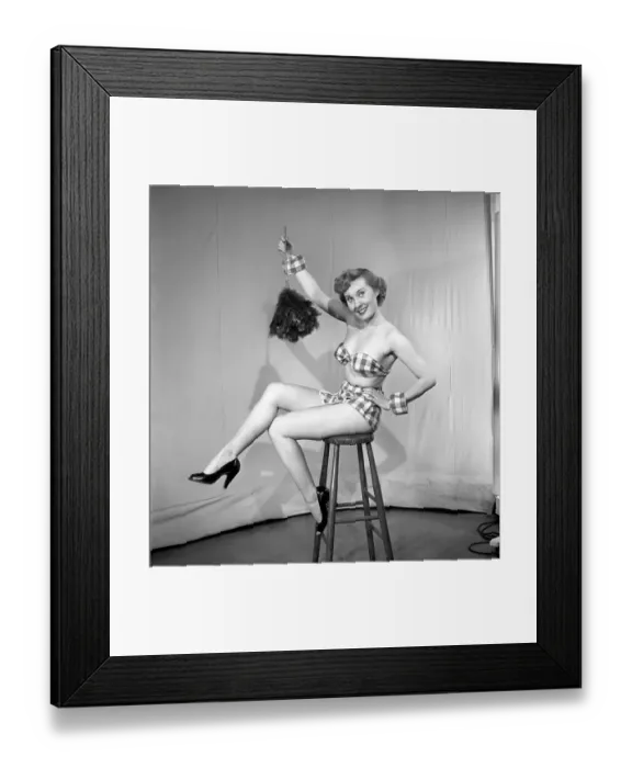 Framed Print : Woman wearing plaid bra and short skirt holding duster. 1959