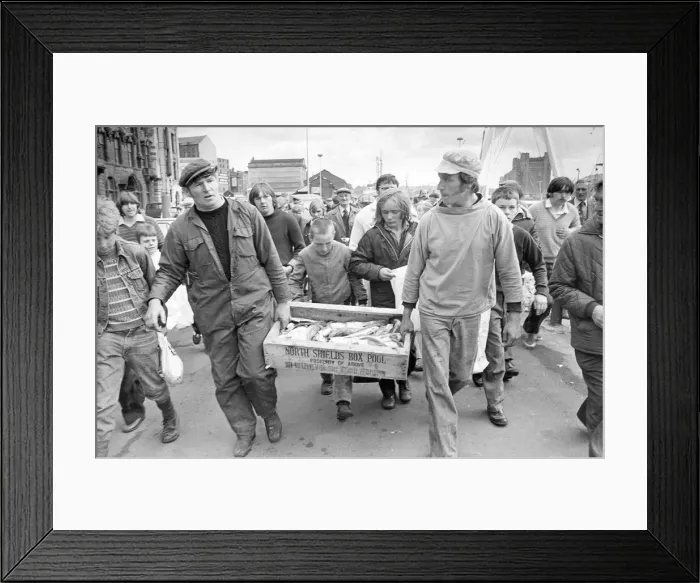 Framed Print : Two fishermen pursued by an eager crowd, bring a box of fish ashore in 1980