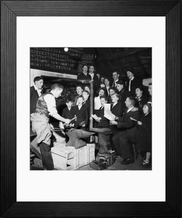 Framed Print : Mr. Simon, smithy and choirmaster, prepares a horseshoe at the anvil while the choir