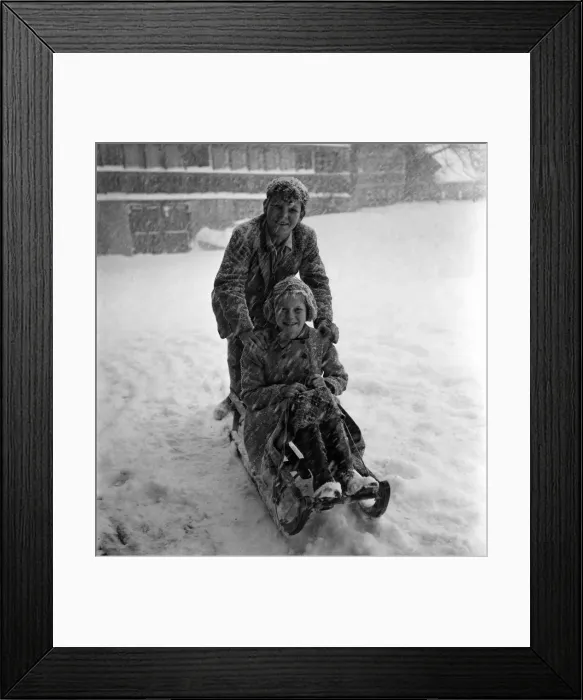 Framed Print : Boy and girl on a wooden sledge in the snow at a resort in Switzerland