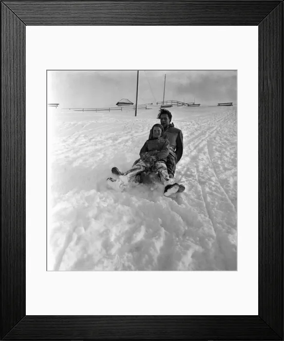 Framed Print : Man and girl on a wooden sledge in the snow at a resort in Switzerland Framed Print : Man and girl on a wooden sledge in the snow at a resort in Switzerland