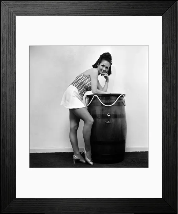 Framed Print : Woman wearing a patterned top and short skirt posing with a barrel