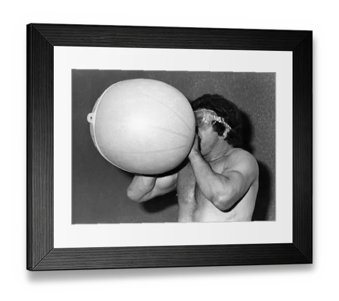 Framed Print : Male stripper Mel blowing up a hot water Bottle. June 1977 P018597