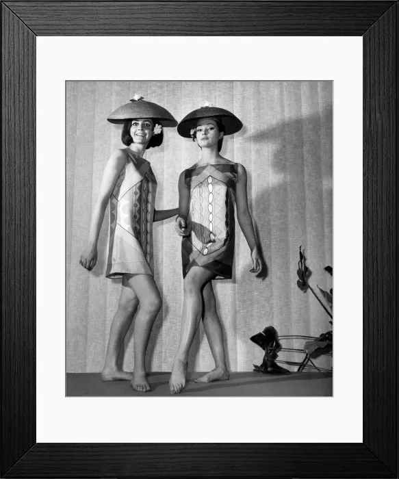Framed Print : Clothing Beach. Two women model patterned mini dresses and lampshade-shaped hats on stage Framed Print : Clothing Beach. Two women model patterned mini dresses and lampshade-shaped hats on stage