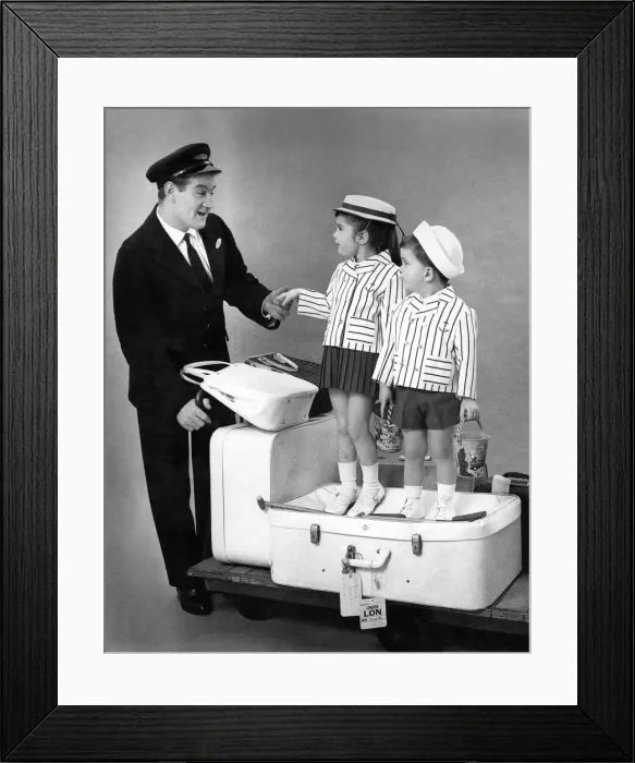 Framed Print : Fashion 1960s. Porter or train conducter wheels children on a trolley with their