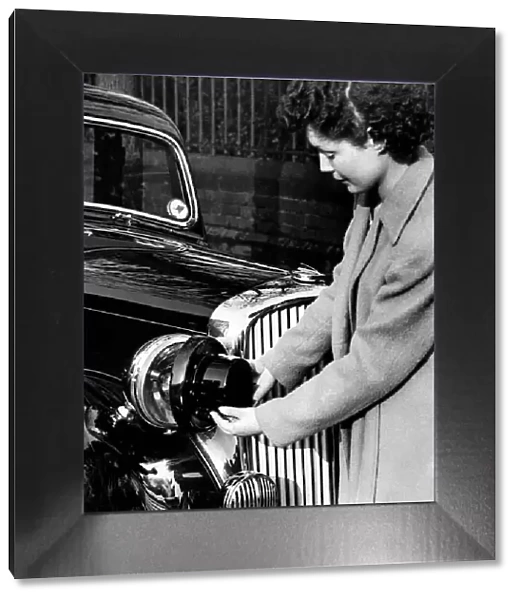 World War II: Blackout. Woman fitting blackout shields to the headlamps of her car