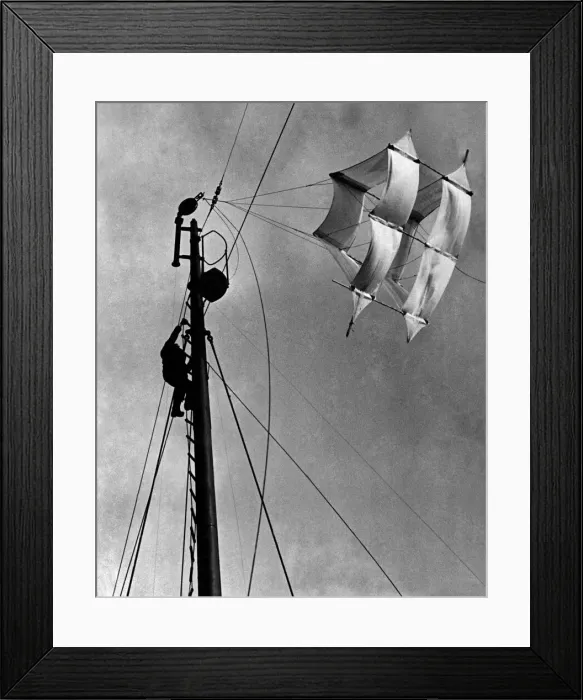 Framed Print : A seaman up the main mast adjusting the huge kite that carries a slender cable Framed Print : A seaman up the main mast adjusting the huge kite that carries a slender cable