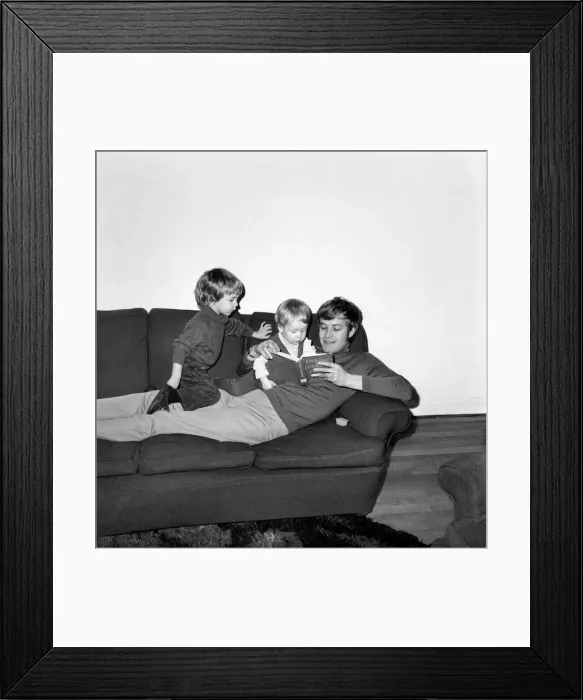 Framed Print : Families: Mother, father and children. Father reading a story to his baby boy on his sofa