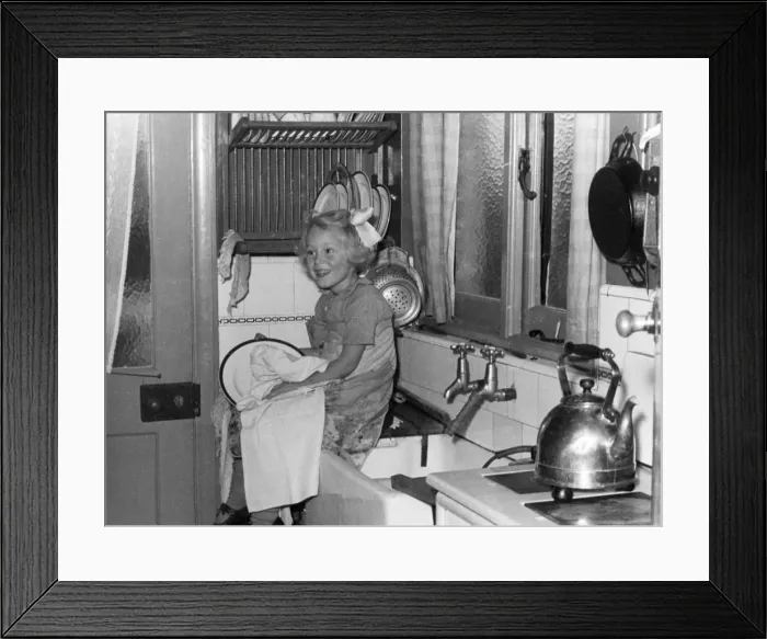 Framed Print : Young girl sitting on the kitchen worktop drying dishes after doing the washing up Framed Print : Young girl sitting on the kitchen worktop drying dishes after doing the washing up