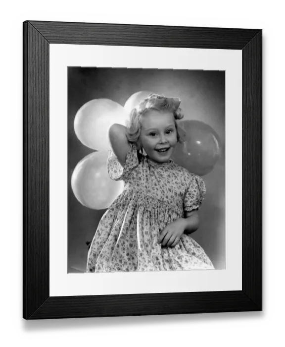 Framed Print : Young girl holding balloons for a party wearing floral patterned dress Circa 1945 Framed Print : Young girl holding balloons for a party wearing floral patterned dress Circa 1945
