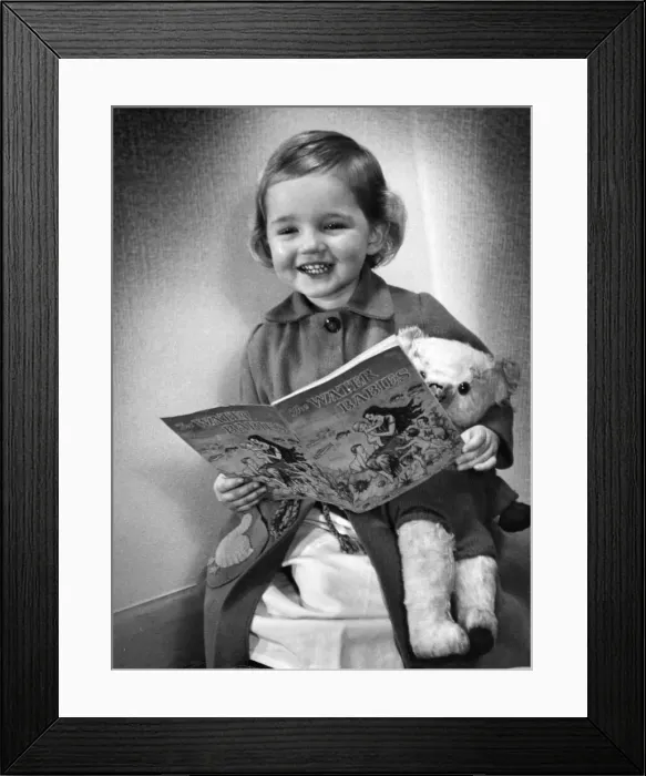 Framed Print : Young girl smiling as she reads her Water Baies book Circa 1945 P044490 Framed Print : Young girl smiling as she reads her Water Baies book Circa 1945 P044490