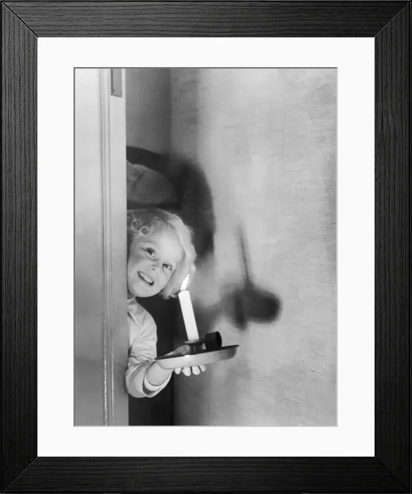 Framed Print : Young girl peering behind a door holding a candle Circa 1945 P044427 Framed Print : Young girl peering behind a door holding a candle Circa 1945 P044427