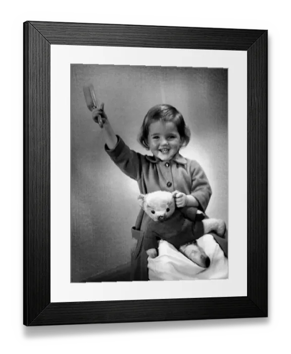 Framed Print : Happy young girl holding up her hairbrush after getting her teddy bear clothed Framed Print : Happy young girl holding up her hairbrush after getting her teddy bear clothed