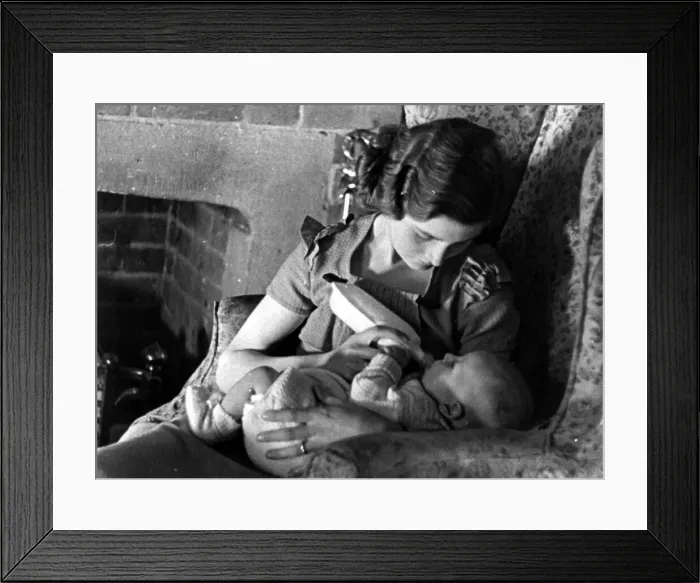 Framed Print : Young mother feeding her baby with a bottle of milk beside the fireplace Circa 1945
