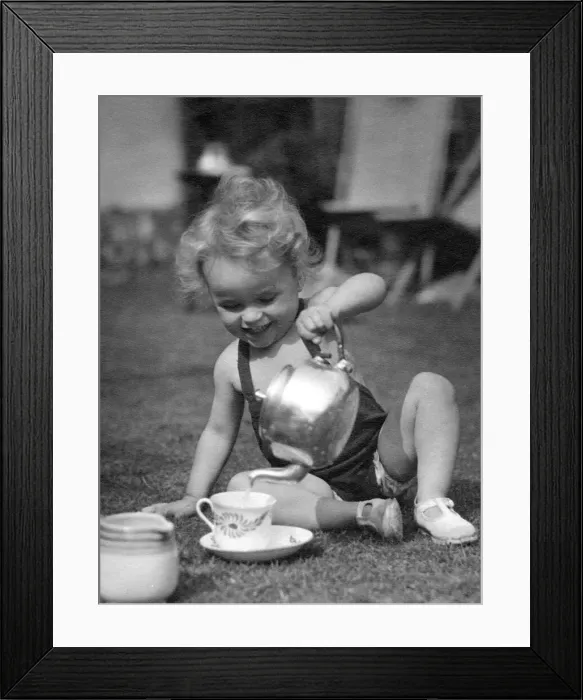 Framed Print : Young child pouring a cup of tea using a kettle in the back garden Circa 1945 Framed Print : Young child pouring a cup of tea using a kettle in the back garden Circa 1945