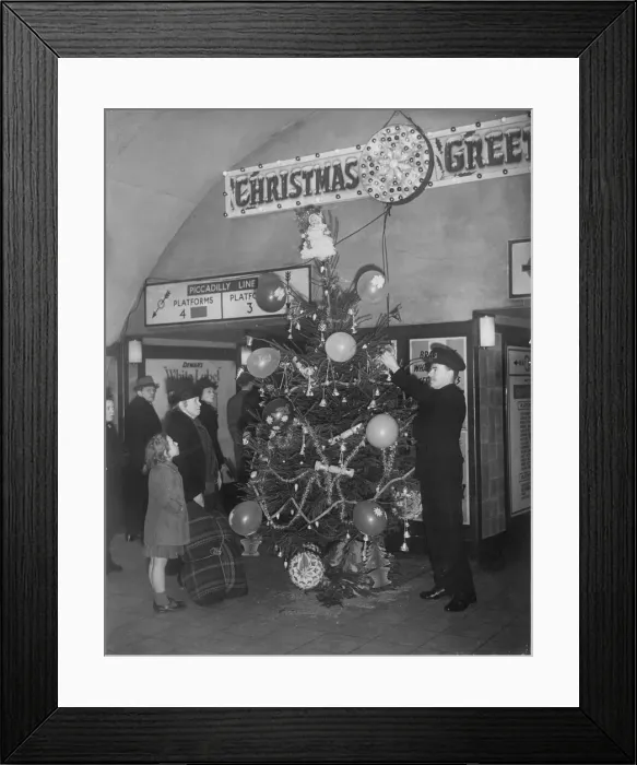 Framed Print : An underground railway guard decorating a Christmas tree at Holburn tube station during Framed Print : An underground railway guard decorating a Christmas tree at Holburn tube station during