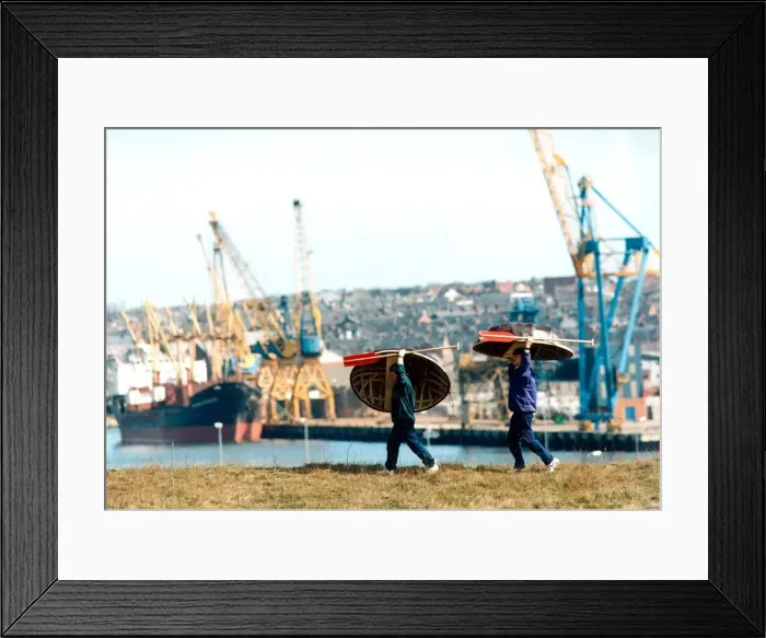 Framed Print : Old and new, Danny Gilchrist and Dave Potts carry thier coracles with a backdrop of Framed Print : Old and new, Danny Gilchrist and Dave Potts carry thier coracles with a backdrop of