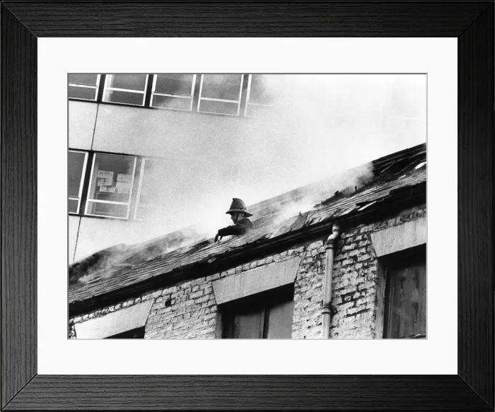 Framed Print : A firefighter pokes his head through the roof of the smoke filled building to grab some Framed Print : A firefighter pokes his head through the roof of the smoke filled building to grab some