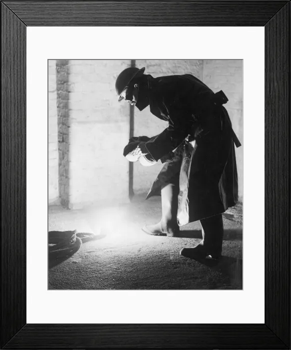Framed Print : A firefighter tackles an incendary bomb with a sandbag which protects his face from Framed Print : A firefighter tackles an incendary bomb with a sandbag which protects his face from