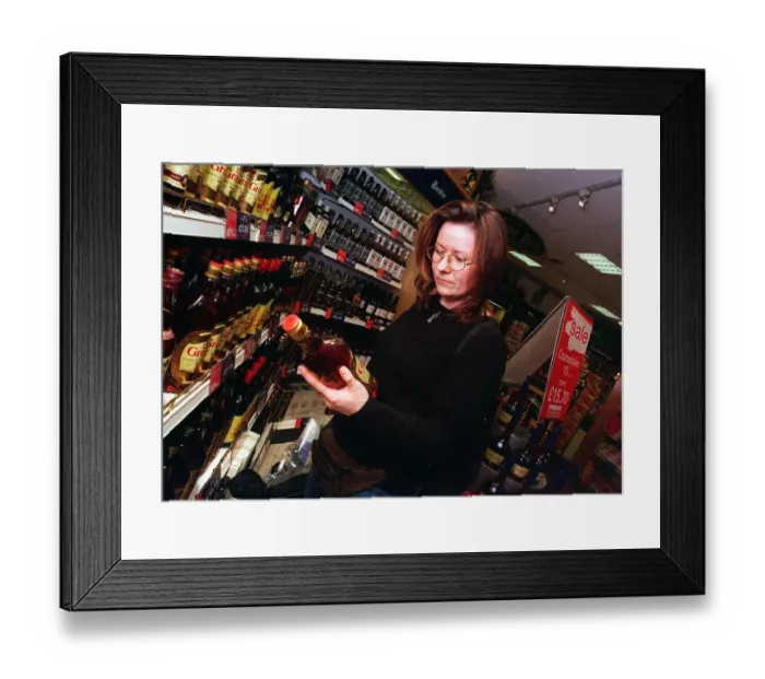 Framed Print : Duty free shop at Edinburgh airport February 1999 Woman looking at bottle of spirits