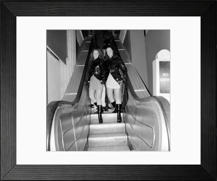 Framed Print : Two women lift up their maxi coats on an escalator in a Liverpool store Framed Print : Two women lift up their maxi coats on an escalator in a Liverpool store