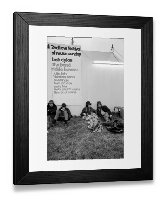 Framed Print : Music fans at The Isle of Wight Festival with a poster of Artists performing behind Framed Print : Music fans at The Isle of Wight Festival with a poster of Artists performing behind