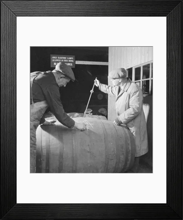 Framed Print : A supervisor at the Glenlivet Distillery measures the contents of barrels of their Framed Print : A supervisor at the Glenlivet Distillery measures the contents of barrels of their