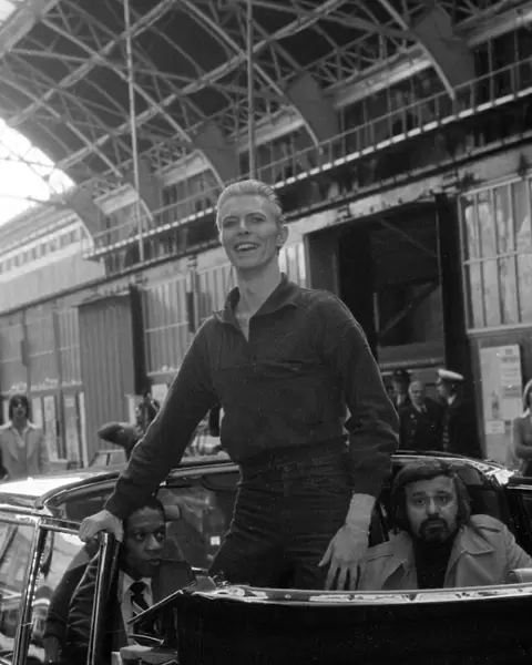 Pop singer David Bowie smiles as he arrives at Victoria Station in London May 1976