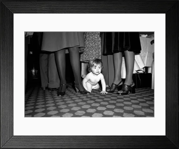 Framed Print : A young baby seen here crawling between the legs of adults at a gathering of them parents