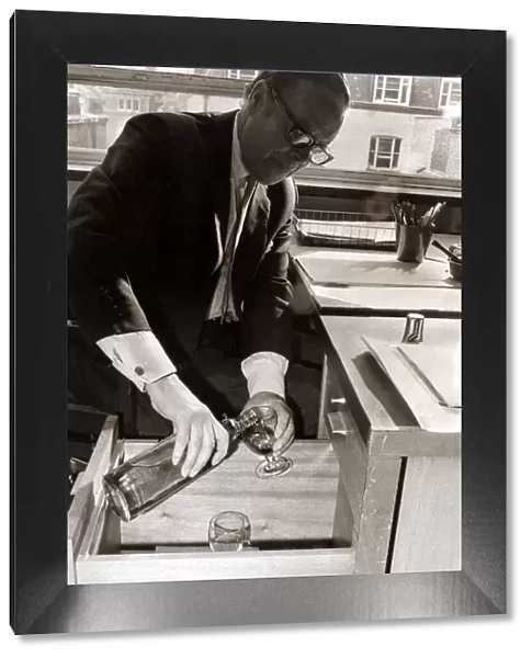 A man pours himself a drink which he keeps hidden in a filing cabinet in his office at