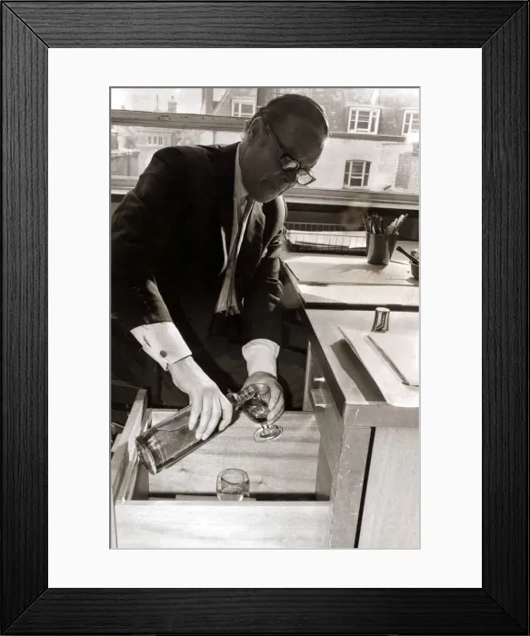 Framed Print : A man pours himself a drink which he keeps hidden in a filing cabinet in his office