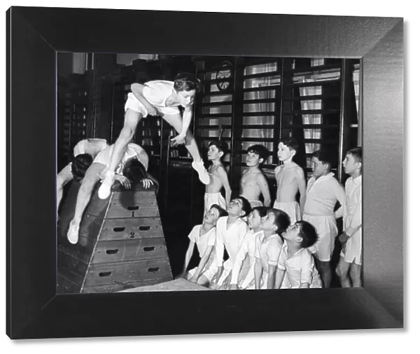 A group of youngsters watch as Richard McKenzie does a astride vault in the gymnasium at