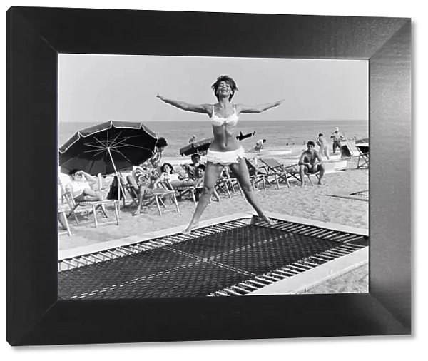 A model wearing bikini swimwear bounces on a trampoline on a beach in the French Riviera
