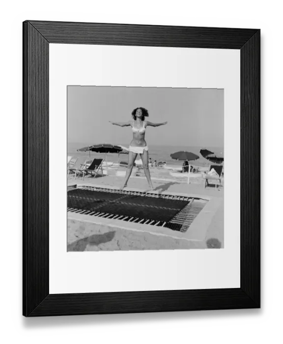Framed Print : A model wearing bikini swimwear bounces on a trampoline on a beach in the French Riviera Framed Print : A model wearing bikini swimwear bounces on a trampoline on a beach in the French Riviera